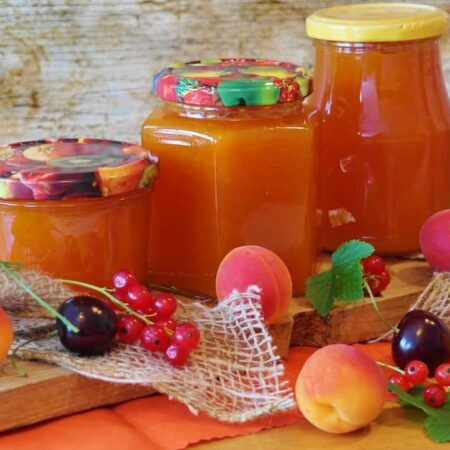 Domáci marhuľový lekvár v pohároch na drevenom stole, vedľa čerstvých marhúľ a lyžice s lekvárom.