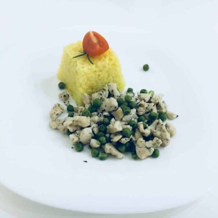 Tanier s kuracími prsiami na hrášku a porciou ryže ozdobenou cherry paradajkou.