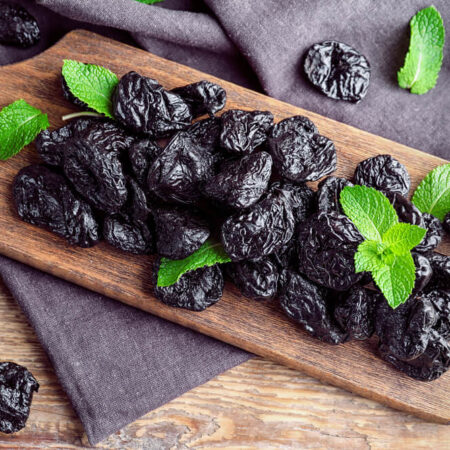 Sušené slivky na drevenej doske, ozdobené čerstvými lístkami mäty.