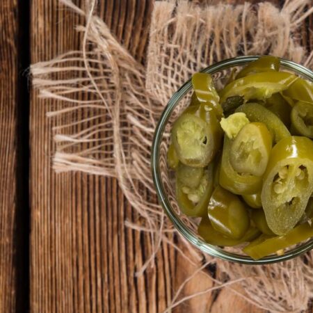 Nakladané jalapenos papričky v sklenenej miske na drevenom stole s rustikálnou dekoráciou.