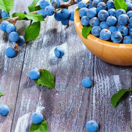 Miska plná čerstvých trniek na drevenom stole s roztrúsenými bobuľami a zelenými listami.