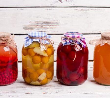 Domáce zaváraniny v sklenených pohároch s farebnými vrchnákmi na drevenom pozadí