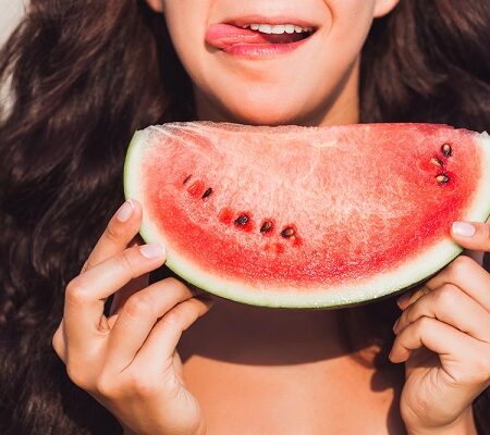 Ovocie a zelenina počas horúčav. Žena drží plátok červeného melónu blízko tváre