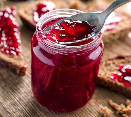 Ringlotový džem: Pohár s domácim ringlotovým džemom a plátky chleba natreté džemom na drevenom stole.