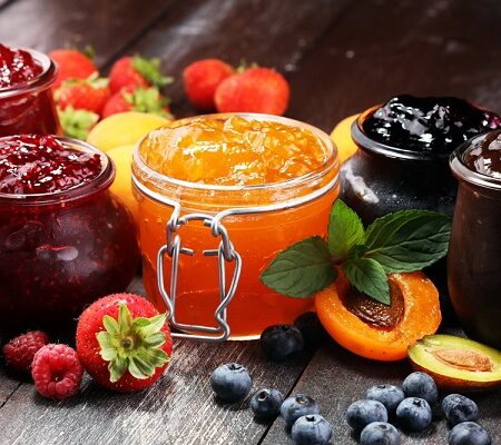 Rôzne druhy ovocných zaváranín v pohároch: lekvár, džem a marmeláda obklopené čerstvým ovocím.
