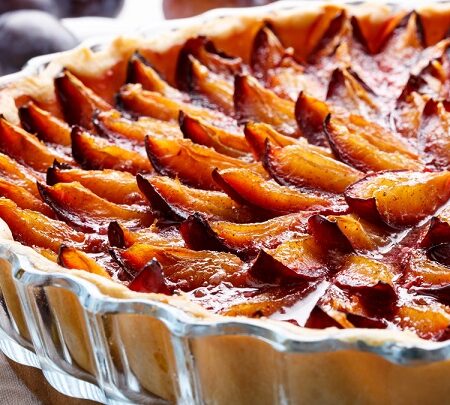 „Blízky pohľad na pečený slivkový koláč v sklenenej forme, s karamelizovanými slivkami úhľadne rozloženými na zlatistom ceste.