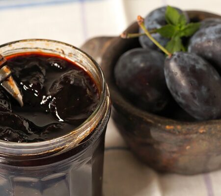 Tradičný pravý slivkový lekvár v skle s drevenou lyžičkou a vedľa misky so slivkami.