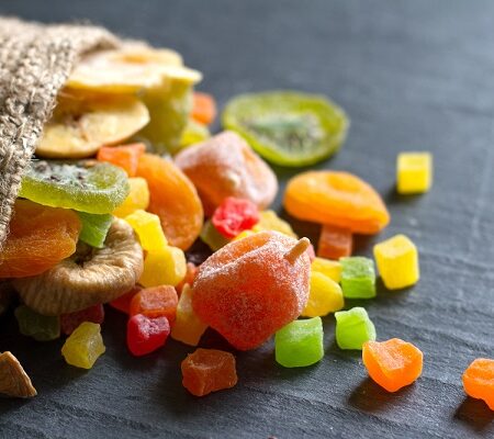 Domáce kandizované ovocie: Rôzne druhy farebného kandizovaného ovocia vylejúce sa z jutového vrecka na tmavý povrch.