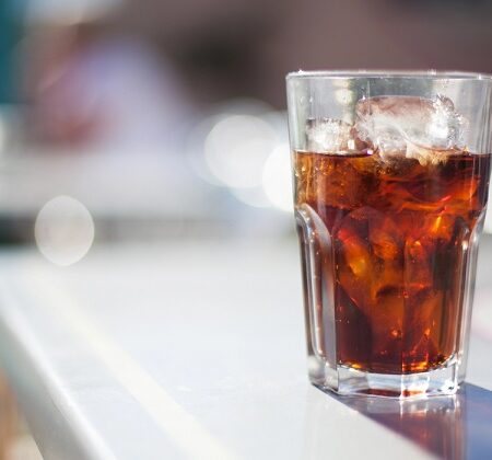 Priemyselné využitie Coca-Coly: Pohár Coca-Coly s ľadom, osviežujúci nápoj na stole s rozmazaným pozadím.