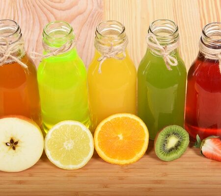 príprava ovocných štiav. Rôzne druhy ovocných štiav v sklenených fľašiach s plátkami ovocia – jablko, citrón, pomaranč, kivi a jahoda.