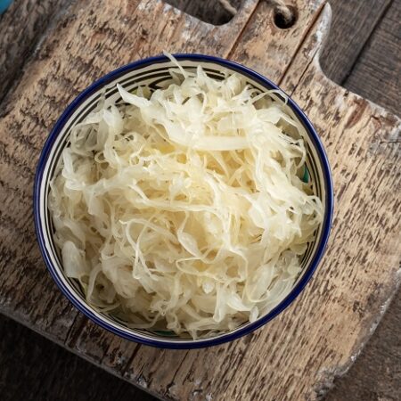 Čerstvá kvasená kapusta v miske na drevenej doske.