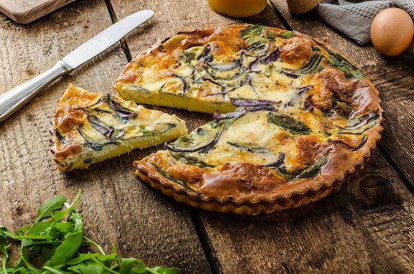 Zeleninový quiche s cibuľou a špenátom na drevenom stole, nakrájaný na trojuholníky.