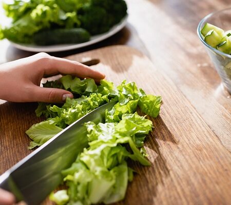 Sterilizovaný hlávkový šalátČerstvý hlávkový šalát sa krája na drevenú dosku spolu s nakrájanými uhorkami v sklenenej mise.