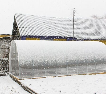 Zimný skleník pokrytý snehom na záhrade, pripravený na vykurovanie počas zimných mesiacov. Ako vykurovať skleník?