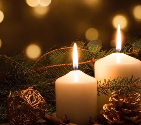 Dve horiace magické sviečky s vianočnými dekoráciami, šiškami a vetvičkami v jemnom zlatom svetle.