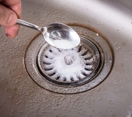 Domáci čistič oodtokov: Ruka nasýpa jedlo sódu do kuchynského odtoku ako súčasť ekologického zásobovania potrubia.