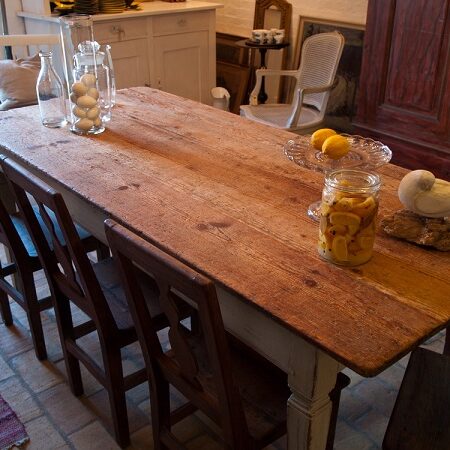 Rustikálny drevený nábytok - stôl s vintage stoličkami, dekorovaný sklenenými fľašami a miskou s ovocím v tradičnej kuchyni