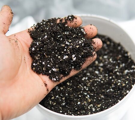 Ruka držiaca substrát s pomocnými pôdnymi látkami v kvetináči, pripravený na výsadbu rastlín. Pôdne látky