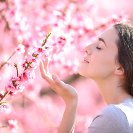jarné vône, trendy Žena si vychutnáva vôňu jarných ružových kvetov v rozkvitnutej záhrade počas slnečného dňa.