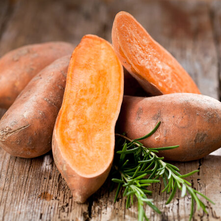 Prekrojené sladké zemiaky s oranžovou dužinou na drevenom stole