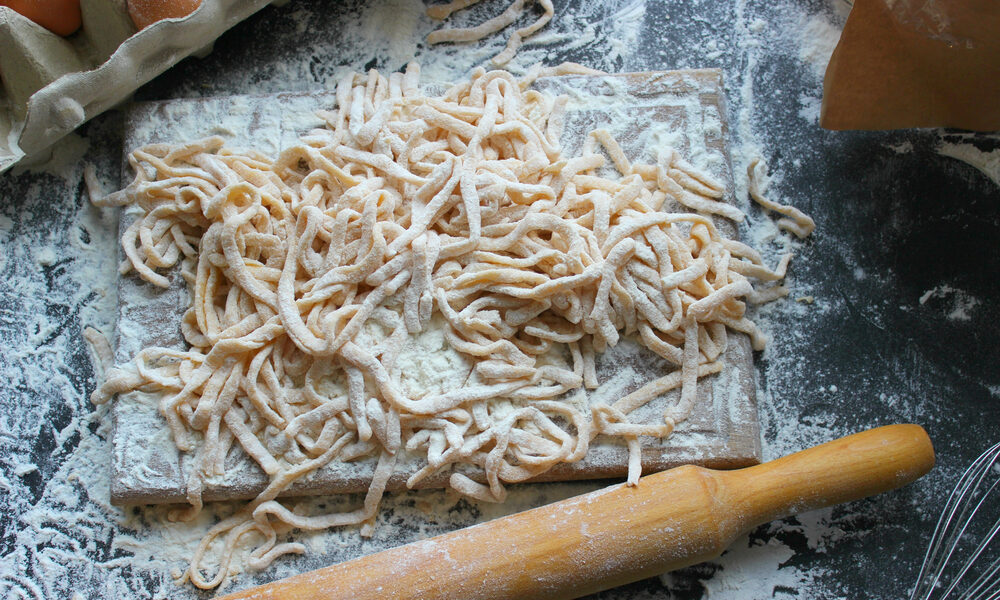 Domáce rezance pripravené na doske posypanej múkou s vajíčkami a valčekom