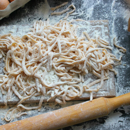 Domáce rezance pripravené na doske posypanej múkou s vajíčkami a valčekom