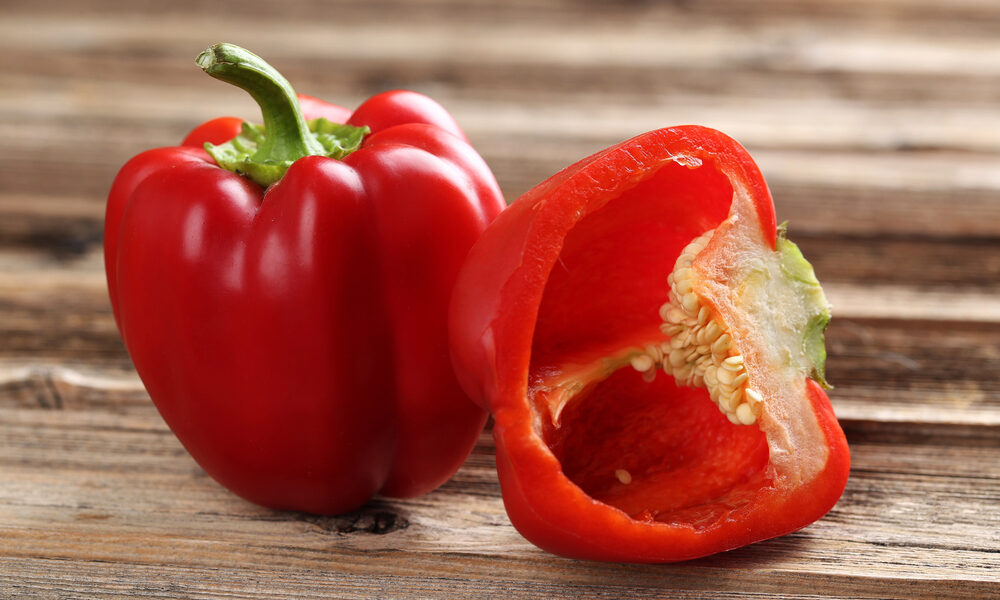 Zrelé semená papriky. Celá červená paprika a rozkrojený plod s viditeľnými svetlými semenami na drevenom stole.